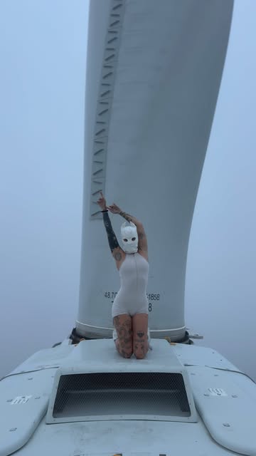Casper in a white balaclava kneeling on the nacelle of a wind turbine in heavy fog